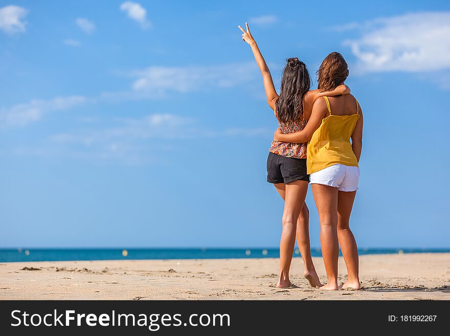 Complicity moment beetwen two girls best friends at the beach. Beautiful young women facing the sea. Complicity moment beetwen two girls best friends at the beach. Beautiful young women facing the sea