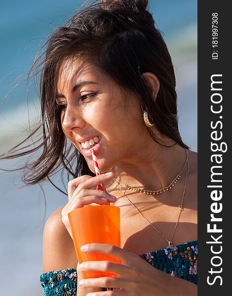Portrait of a beautiful brunette drinking cocktail while standing on beach. Summer vacation concept. Happy girl enjoying freedom. Portrait of a beautiful brunette drinking cocktail while standing on beach. Summer vacation concept. Happy girl enjoying freedom