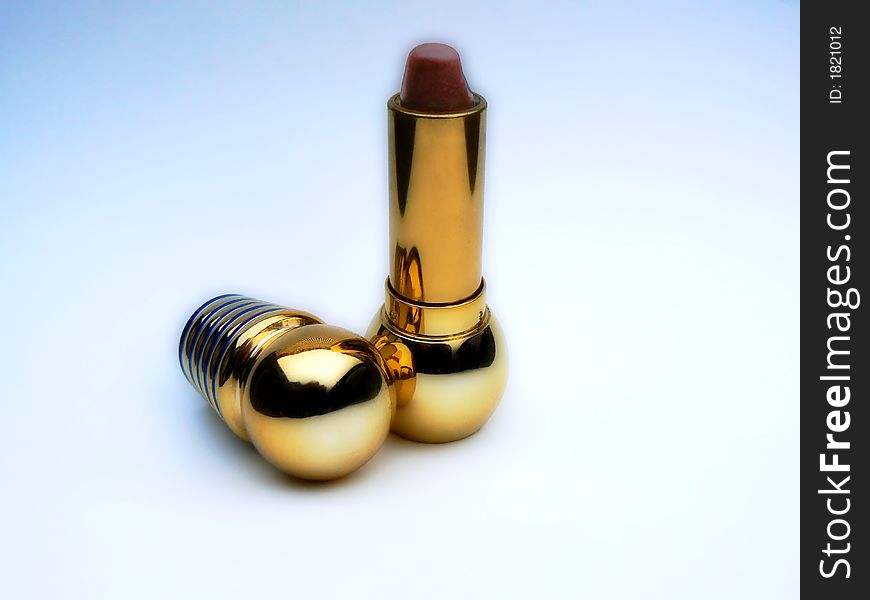 Open golden case with dark-red lipstick over bluish background. Open golden case with dark-red lipstick over bluish background