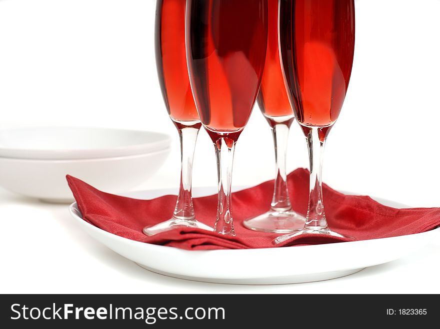 Four glasses of rose champagne on a red napkin isolated on white with bowls in background