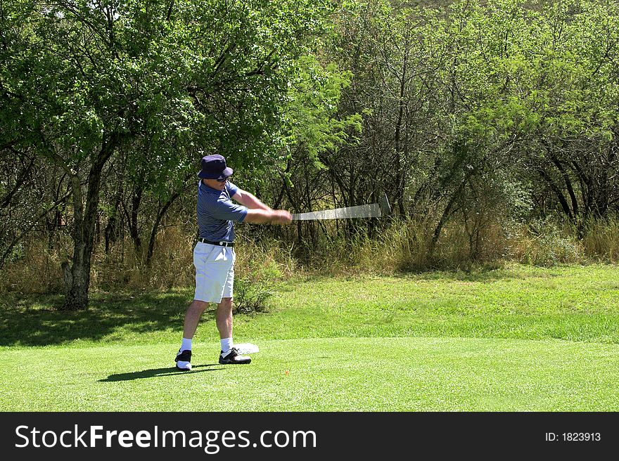Golfer in striped shirt hitting the ball from the tee box. Golf club and arms of the golfer are in motion. . Golfer in striped shirt hitting the ball from the tee box. Golf club and arms of the golfer are in motion.