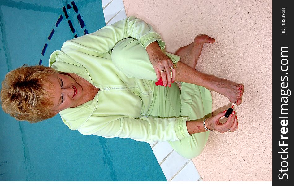 A senior woman painting her toe nails by the pool. A senior woman painting her toe nails by the pool