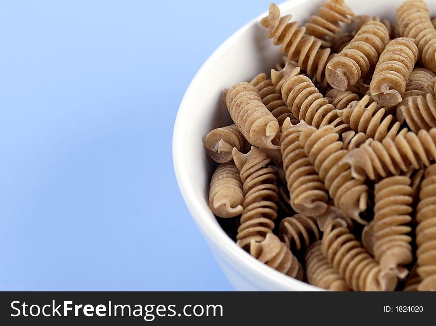 A bowl of wholewheat Rotini Pasta on a fresh, light-blue background. A bowl of wholewheat Rotini Pasta on a fresh, light-blue background.