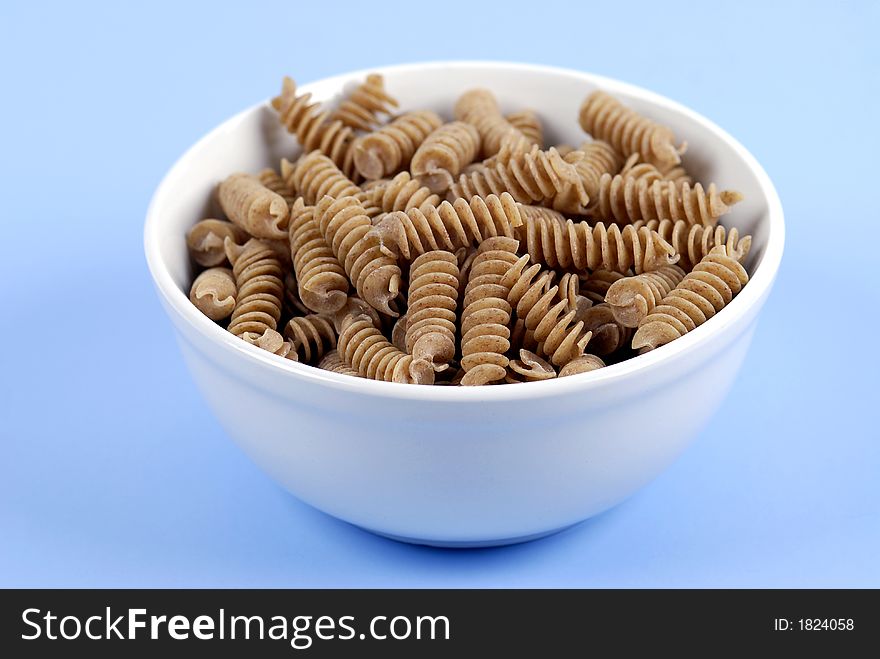 A bowl of wholewheat Rotini Pasta on a fresh, light-blue background. A bowl of wholewheat Rotini Pasta on a fresh, light-blue background.