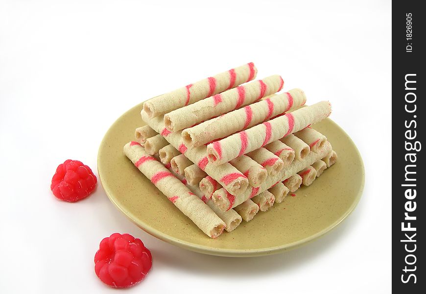 Beautiful cookies as sticks on a plate with fruit candy a raspberry on a white background