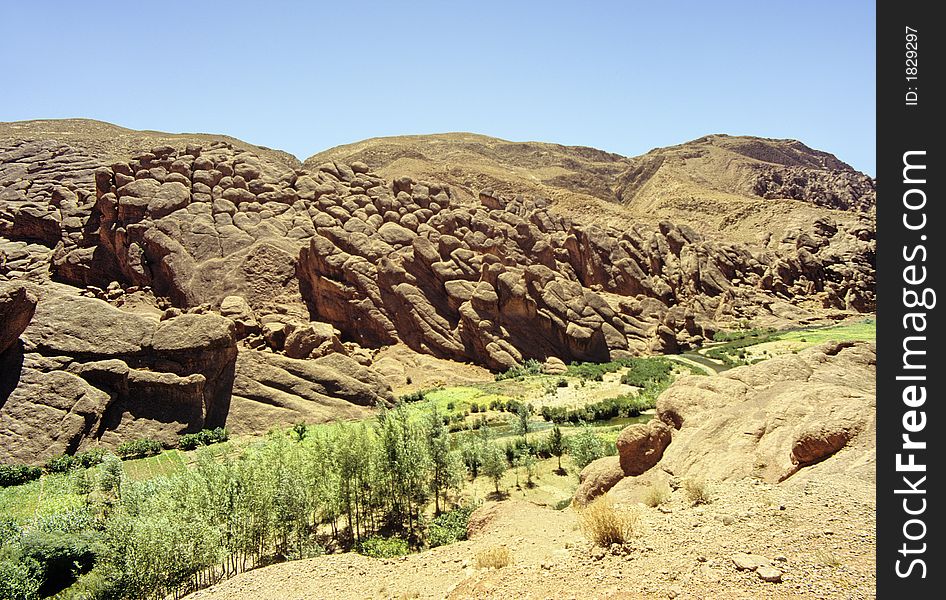 Small valley between sandstone and clay bare cliffs, with narrow meadows and some trees on the riverside in a very dry surroundings. southern Morocco. Small valley between sandstone and clay bare cliffs, with narrow meadows and some trees on the riverside in a very dry surroundings. southern Morocco