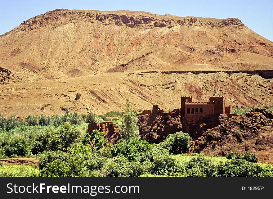 Typical valley in southern Morocco with some green trees and meadows, bare red hills, small clay castle. Typical valley in southern Morocco with some green trees and meadows, bare red hills, small clay castle.