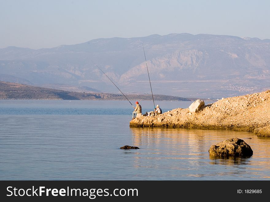 Two fishermen catch fish seafishing in greece  rock coast. Two fishermen catch fish seafishing in greece  rock coast