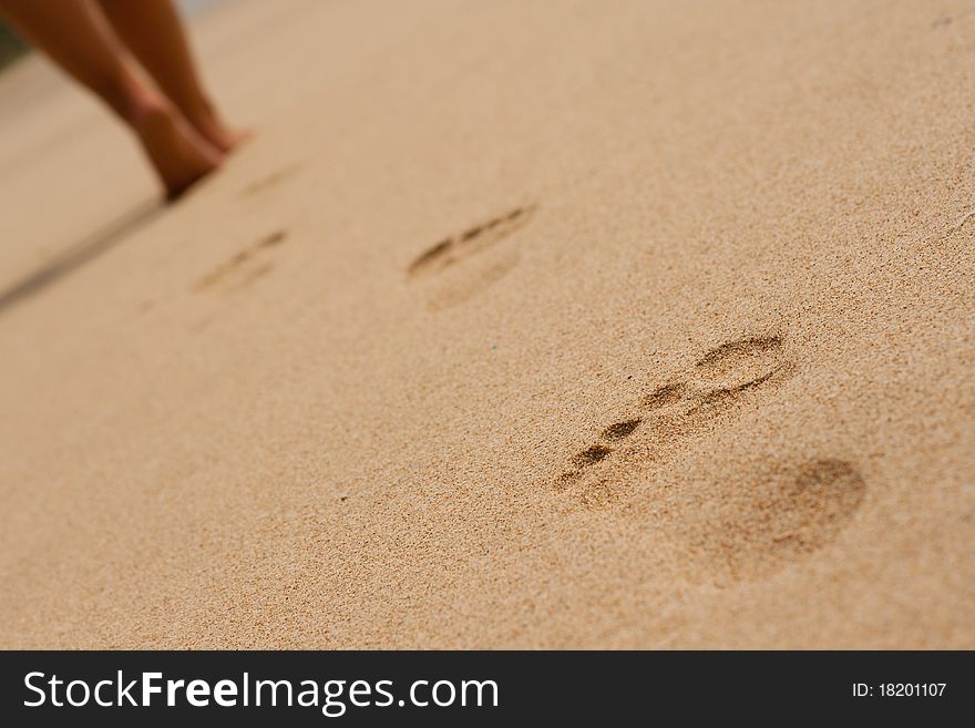 Image of women's legs on the beach and footprints in the sand