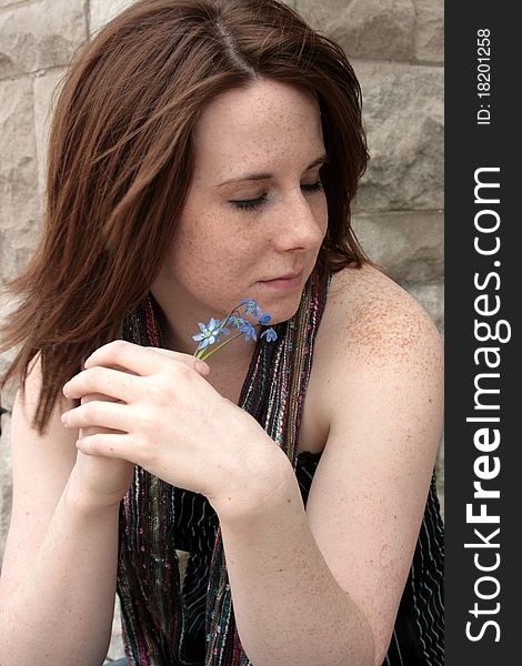 A portrait of a young freckled woman holding a spring of blue flowers. A portrait of a young freckled woman holding a spring of blue flowers.