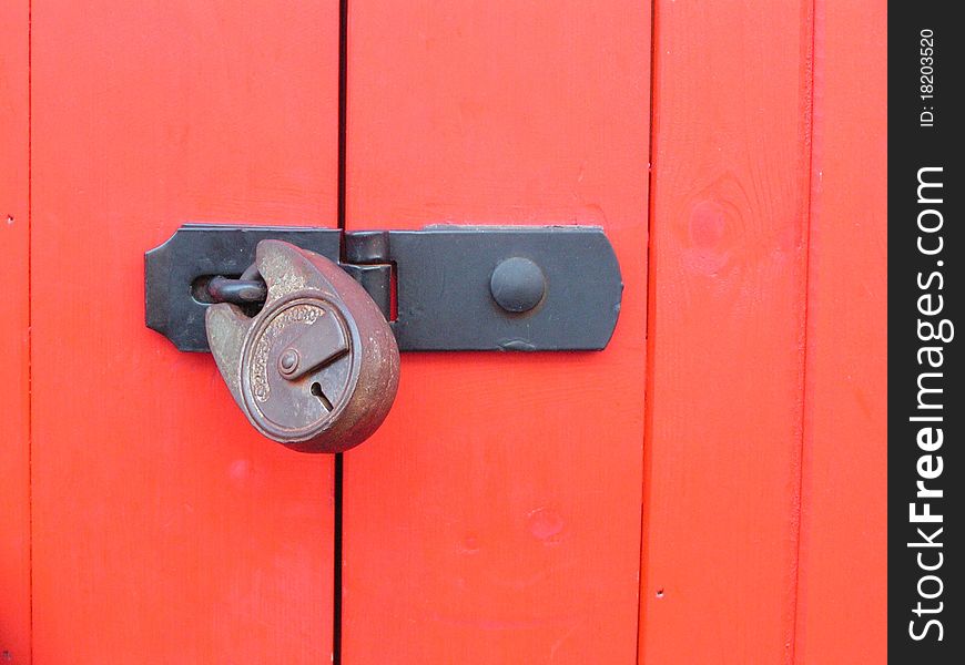 Red painted wooden door closed with a hasp and padlock. Red painted wooden door closed with a hasp and padlock
