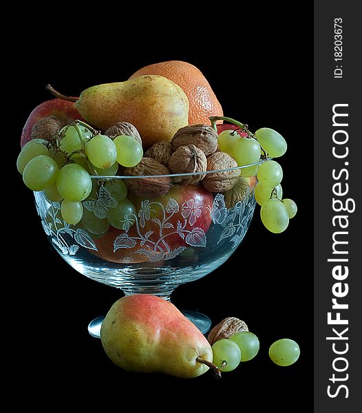 Pears, oranges grapes walnuts displayed in crystal bowl and isolated on black background. Pears, oranges grapes walnuts displayed in crystal bowl and isolated on black background