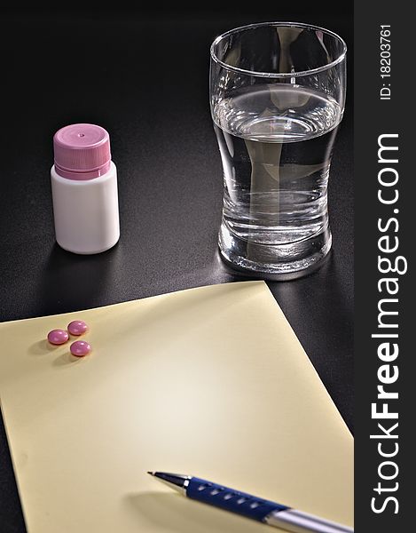 Tablets a glass with water and a paper blank leaf on a black background. Tablets a glass with water and a paper blank leaf on a black background