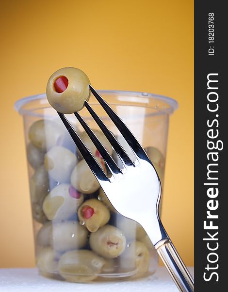 Olives with red pepper in box. Fork in foreground. Studio shot with artistic selective focus. Olives with red pepper in box. Fork in foreground. Studio shot with artistic selective focus