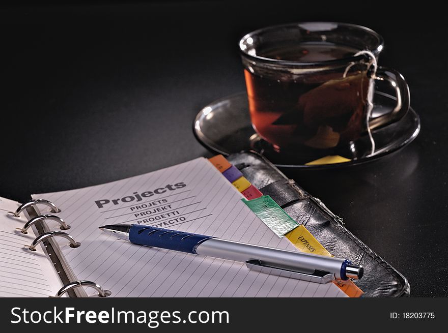 Pen a notebook and a tea cup against a dark background. Pen a notebook and a tea cup against a dark background