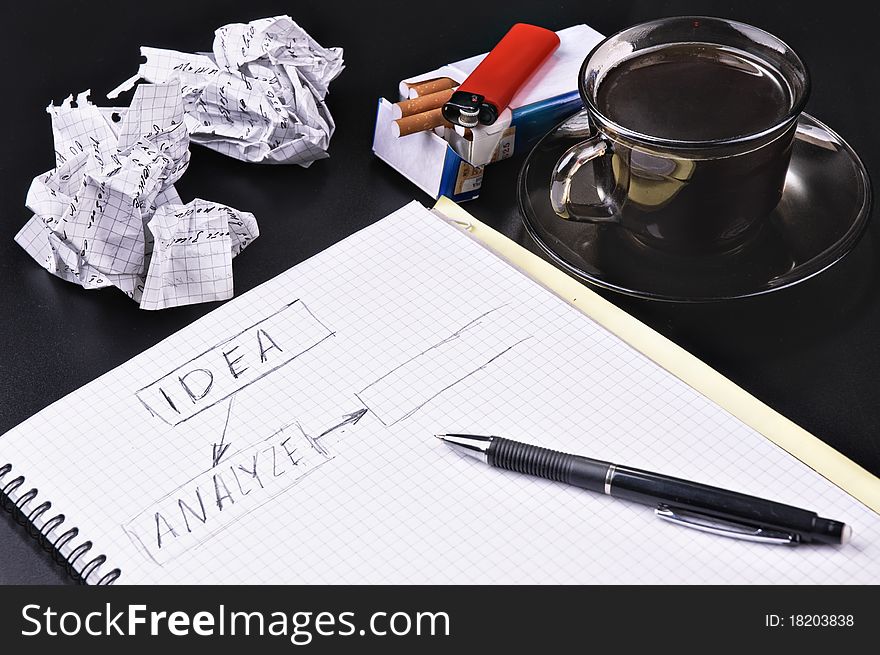 Notebook a pencil the crumpled sheets of a cigarette of coffee against a dark background. Notebook a pencil the crumpled sheets of a cigarette of coffee against a dark background