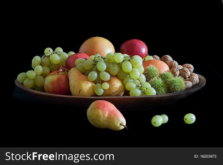 Pears, oranges grapes walnuts, chestnuts in outer covering, displayed in teak wood tray and isolated on black background. Pears, oranges grapes walnuts, chestnuts in outer covering, displayed in teak wood tray and isolated on black background