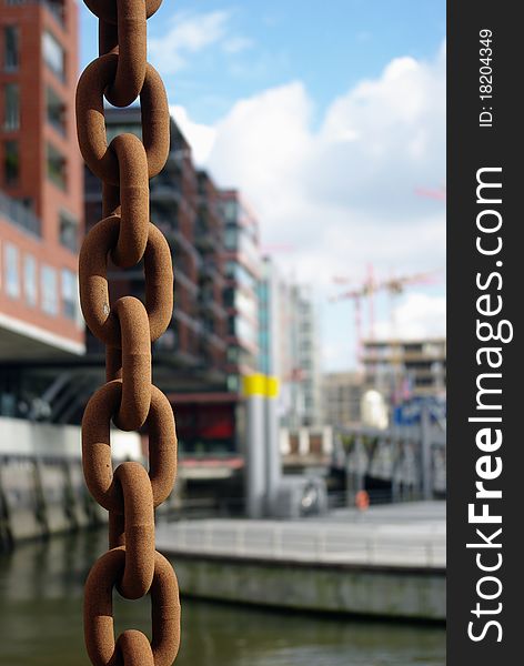 Harbour scene with rusty chain in the foreground, modern architecture and a pier in the background