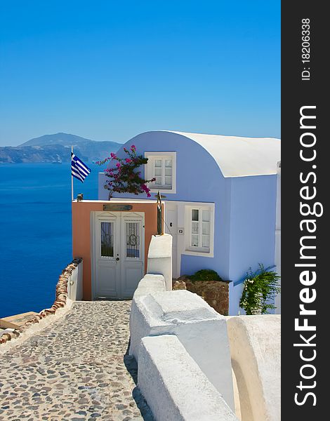 Beautiful house with greece national flag on the street in Santorini, Oia. Aegean sea in a background, Greece. Beautiful house with greece national flag on the street in Santorini, Oia. Aegean sea in a background, Greece.