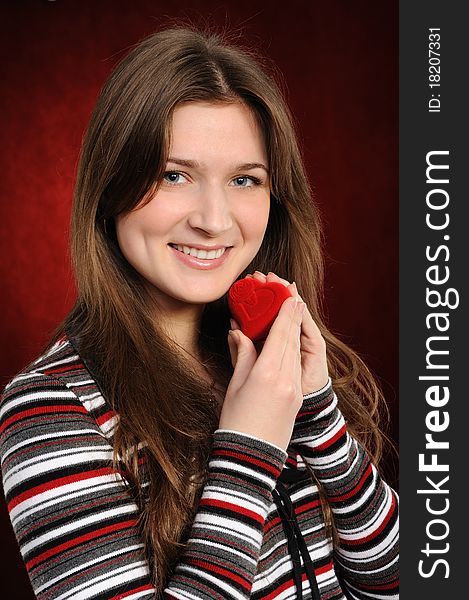 Beautiful woman with a heart gift on the red background