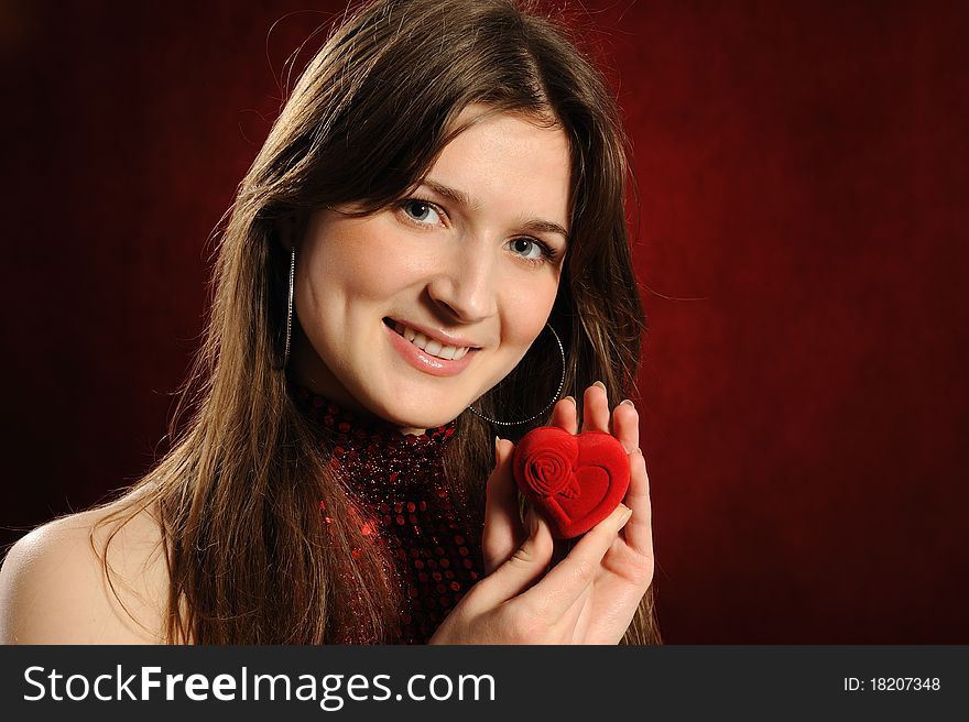 Beautiful woman with a heart gift on the red background