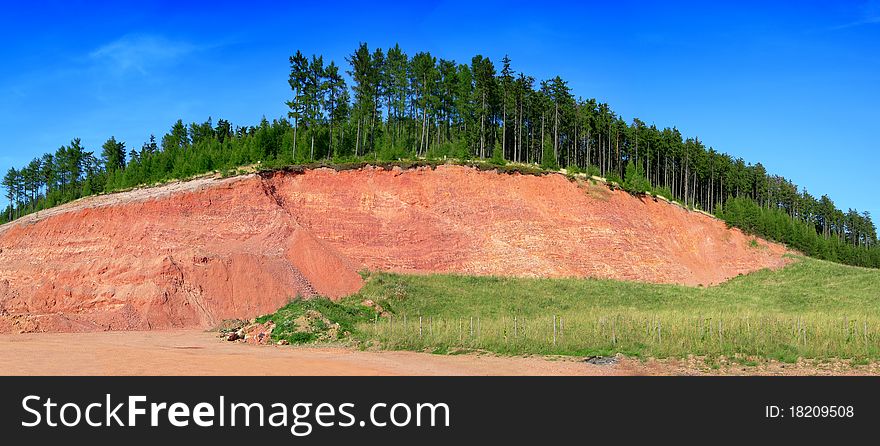 Beautiful panoramic photo of a red hill covered by trees