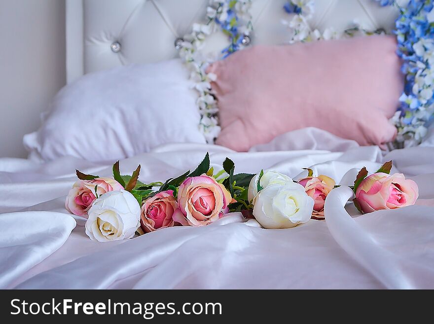 A bouquet of artificial flowers lies on a white silk blanket on a large bed.
