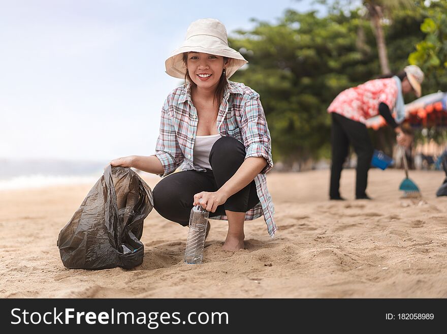 Asian woman picking  bottle into plastic bag black for cleaning the beach in morning time, Volunteer concept.