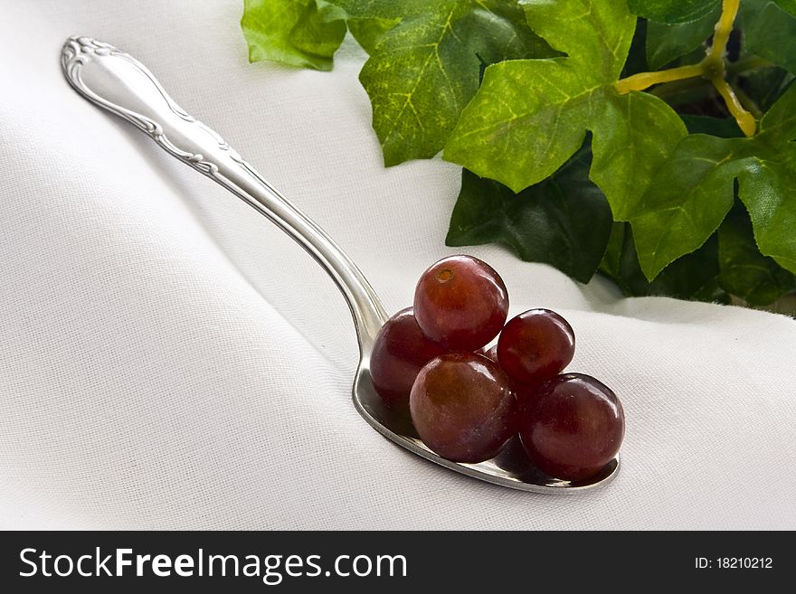 Red grapes piled on spoon on white cloth with leaves on background. Red grapes piled on spoon on white cloth with leaves on background