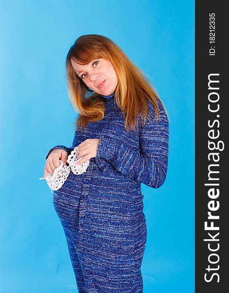 Beautiful pregnant woman with baby's bootees on blue background