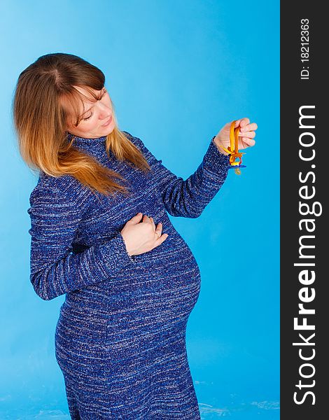 Beautiful pregnant woman with baby's soother on blue background