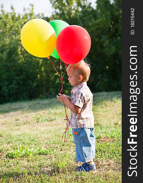 A boy is standing on a lawn with colorful balloons