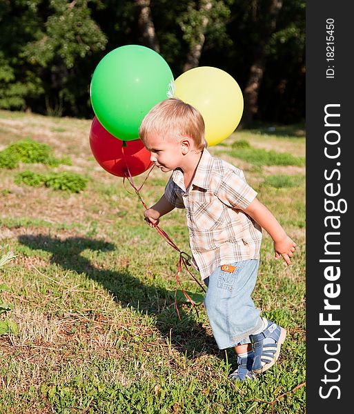 A cute boy is running on a lawn with colorful balloons. A cute boy is running on a lawn with colorful balloons