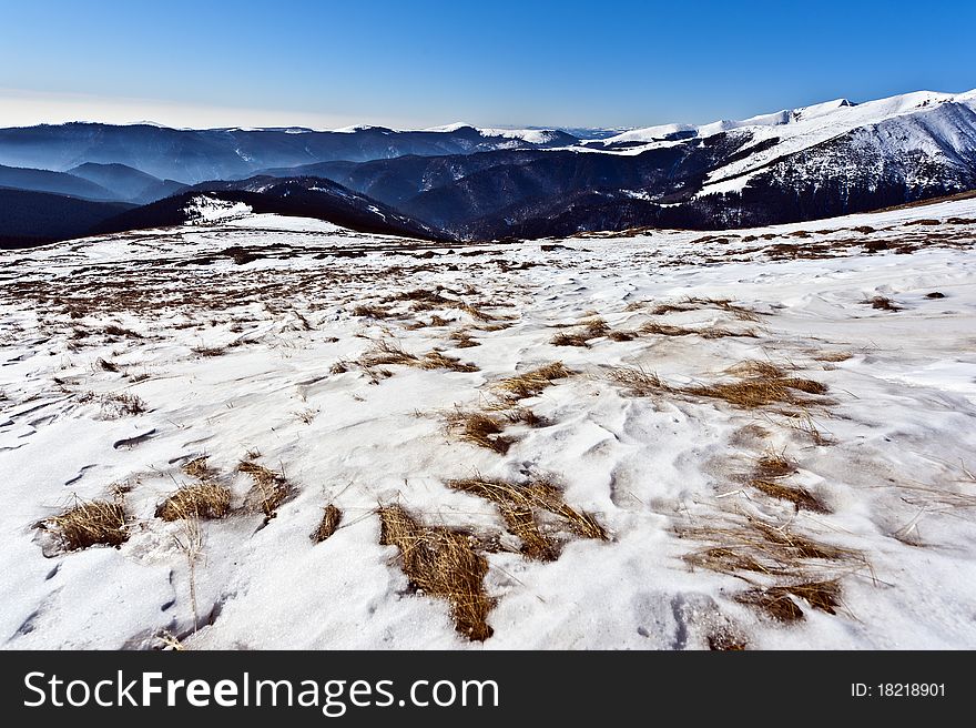 Mountain scenery out of the grass under the snow in the foreground