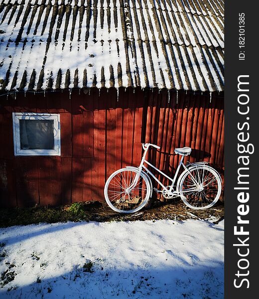 Decorative old painted in white bicycle near farm barn wall on snow