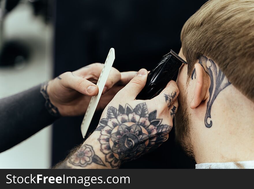 Male Haircut With Electric Razor. Tattooed Barber Makes Haircut For Client At The Barber Shop By Using Hairclipper. Man