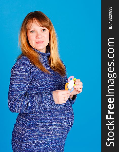 Beautiful pregnant woman with little rattle on blue background