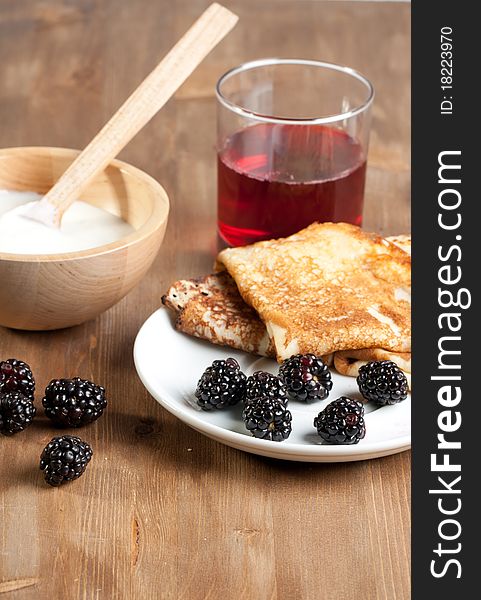 Breakfast with pancakes, yogurt and blackberries, served on wooden table with glass of juice. Breakfast with pancakes, yogurt and blackberries, served on wooden table with glass of juice