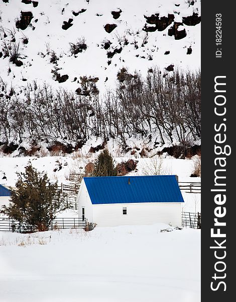 A snowy rural scene of a small farm and white barn with a bright blue roof. A snowy rural scene of a small farm and white barn with a bright blue roof.