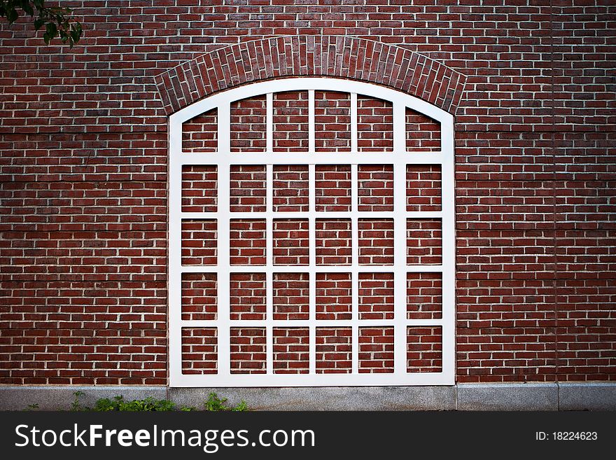 A white window frame topped by an arch, over a red brick wall, seems to be a window to nowhere.