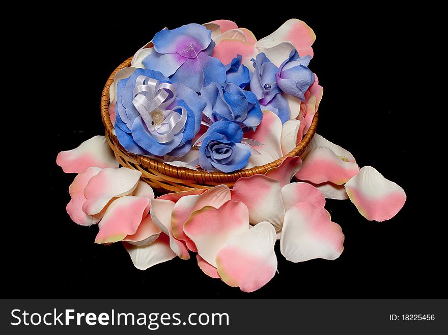 A basket with artificial flowers on white and pink rose textile petals on black. A basket with artificial flowers on white and pink rose textile petals on black