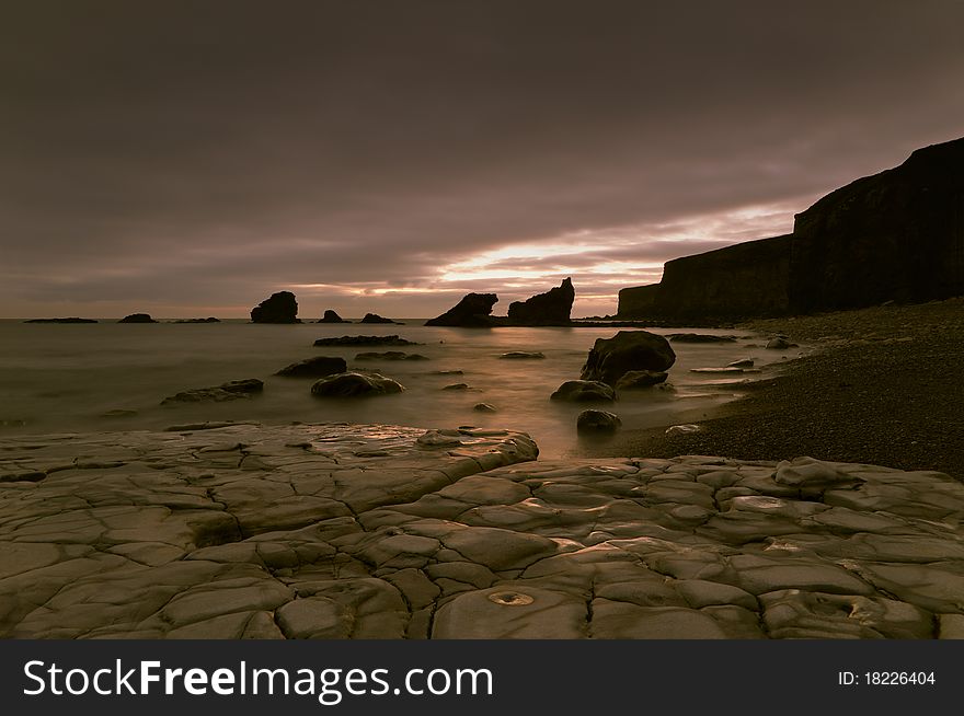 Photograph of a rocky shoreline during an overcast sunrise.