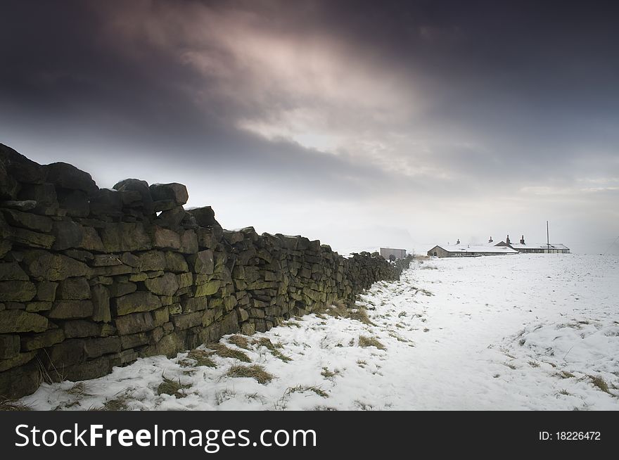 Winter shot of an upland farm and dry stone wall surrounded by snow under a moody sky. Winter shot of an upland farm and dry stone wall surrounded by snow under a moody sky.