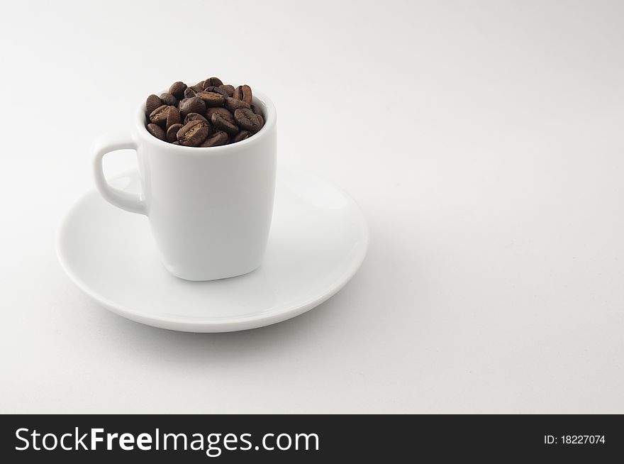 An espresso cup filled with coffee beans sits on a saucer. Photographed against neutral background. An espresso cup filled with coffee beans sits on a saucer. Photographed against neutral background.