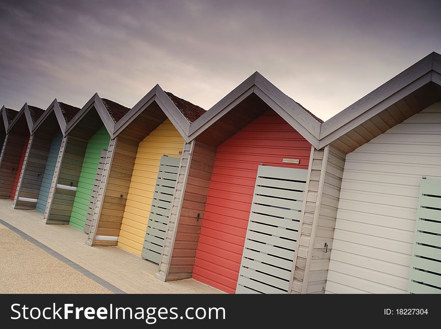 Photograph of colorful beach huts under a slightly moody sky.