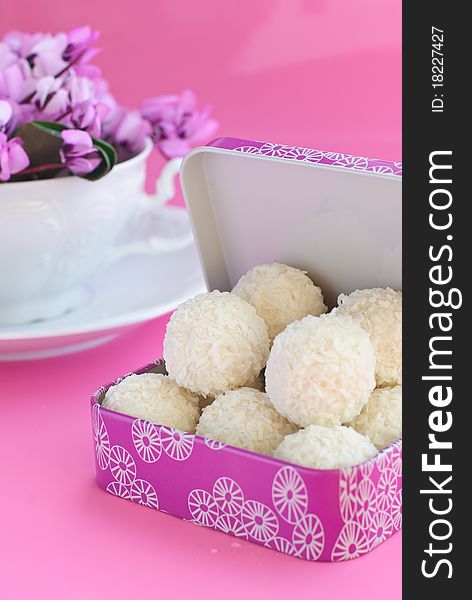White candies into a pink box, white cup with purple spring flowers on pink background. White candies into a pink box, white cup with purple spring flowers on pink background