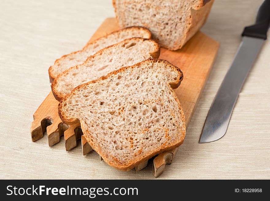 Brown bread slices on a wooden board with knife aside.