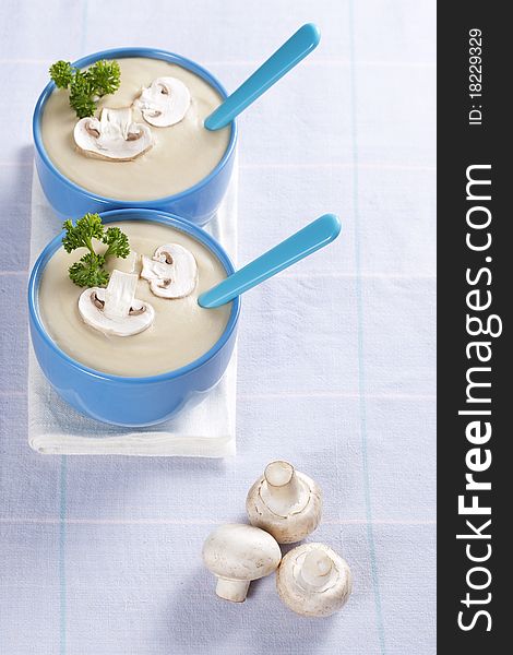 Two bowls of mushroom soup with fresh mushrooms and parsley