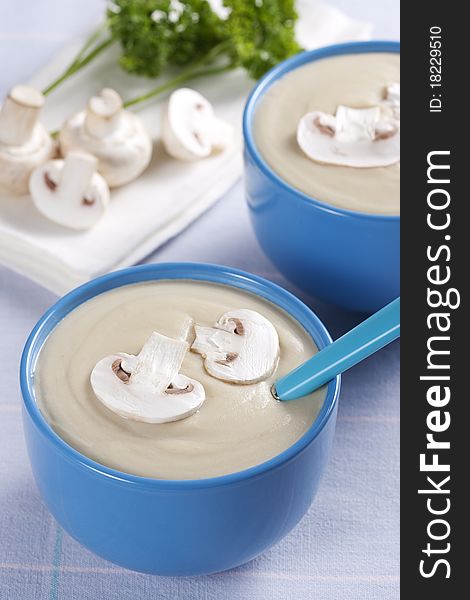 Two bowls of mushroom soup with fresh mushrooms and parsley