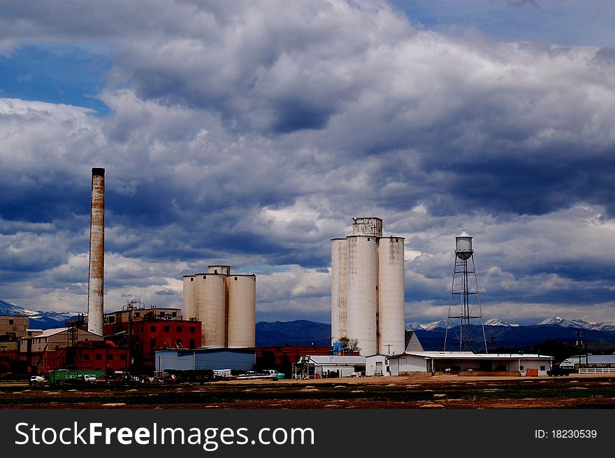 Old factory with blue sky lots of white clouds near boulder Colorado, silos, smoke stacks, water tower and mountains